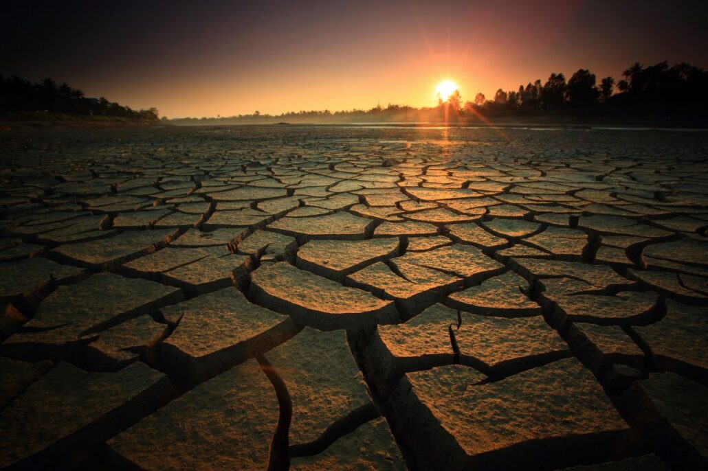 Rio com chão seco por falta de água e sol ao fundo